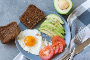 scrambled eggs with avocado and tomato, whole grain bread, fork, knife, towel
