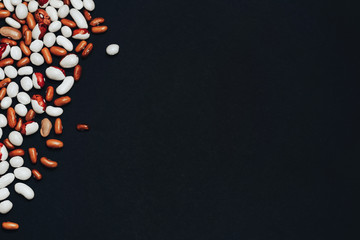 background with space for text. View from above. multi-colored beans scattered on a black background. brown and white beans