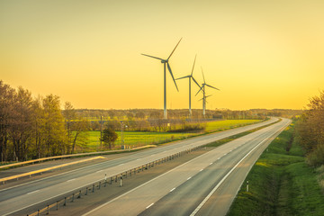 Picture of wind farm generators in the green field close to the road with cars at the sunset