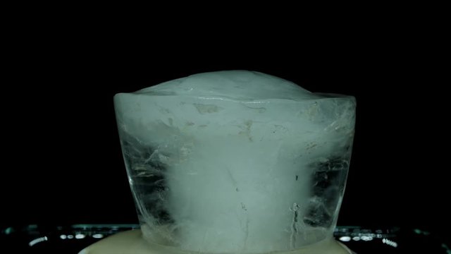 Timelapse closeup shot: a melting ice block over a black background.