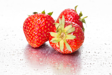 Three ripe strawberries on a white background with water drops. Macro. Close-up.