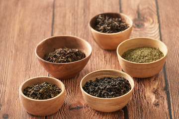 assortment of dry tea in white bowls on wooden surface