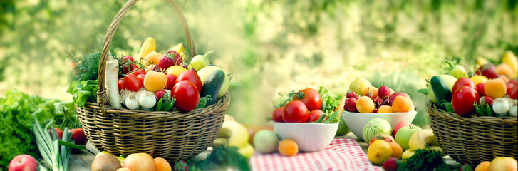 Fresh organic fruits and vegetables in wicker basket and in bowl on table outdoor