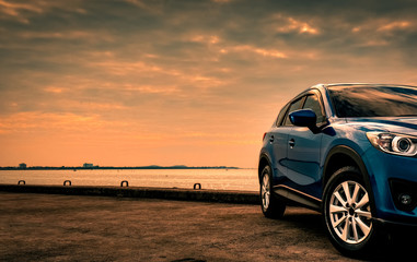 Blue compact SUV car with sport and modern design parked on concrete road by the sea at sunset in...