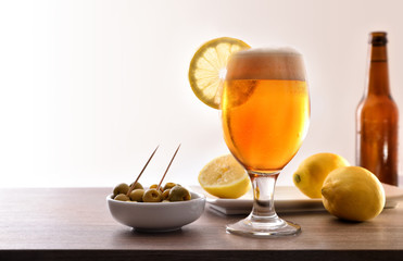 Glass of beer with lemon and appetizer on table white