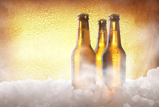 Three full beer bottles on ice and golden background