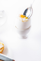 Soft boiled egg in egg cup on white background, plate and cup. Close up. Selective focus. High key.