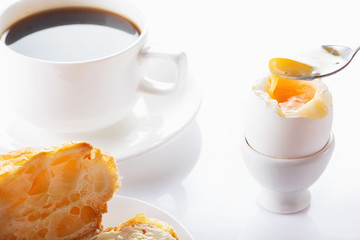 Breakfast. Croissant with butter, coffee and soft-boiled egg. High key. Selective focus.