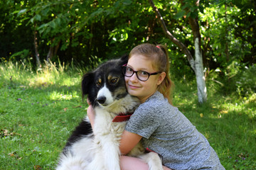Girl playing with dog on grass. Teenager hugging Carpathian Shepherd Dog in the summer park. Friendship concept of man and animal