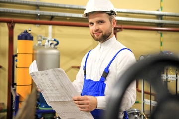 Handsome engineer with blueprints on industrial plant. Man with technical drawings on oil and gas factory