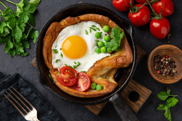 Savory Dutch baby pancake with fried egg, tomato and green peas in cast iron pan