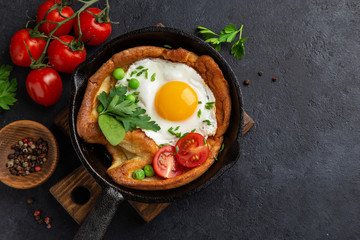 Savory Dutch baby pancake with fried egg, tomato and green peas in cast iron pan