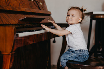 Cute little happy child girl playing piano in a light room. Selective focus, noise effect