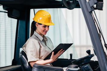 Female worker or inspector sitting at forklift truck looking at document.