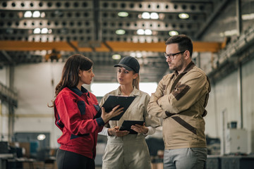 Three industrial workers discussing business at factory hall.