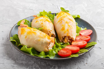 stuffed baked squid with greens on a blue ceramic plate on a gray concrete background, side view.