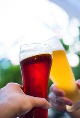 Close-up view of a two glass of beer in hand. Beer glasses clinking at outdoor bar or pub