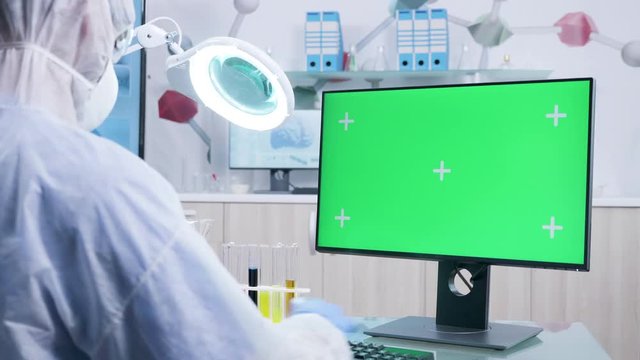 Chemist is white coverall working on green screen computer in modern and secure high end research laboratory