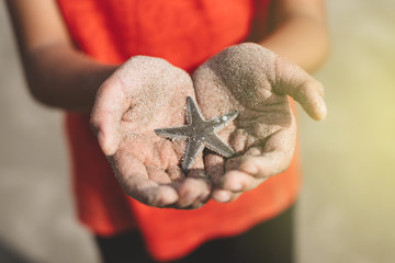 child holding or showing a starfish in a cupped hand with beach sand. concept of marine and aquatic...
