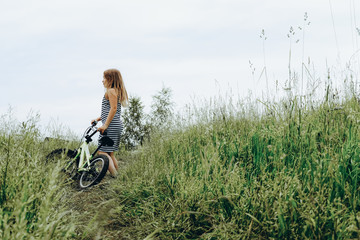 Girl in striped dress riding bike. Spending time outdoors. Child playing outside in spring, summer. Childhood memories. Walking in park, forest. Going on journey, adventure in wilderness