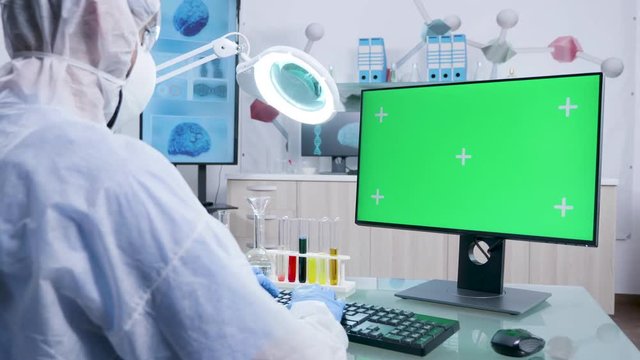 Dolly shot of scientist in white coverall typing on green screen mock-up computer in advanced research laboratory