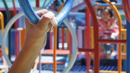 Close up boy hand on blue hanging ring with blurred background of little girl climbing jungle gym in playground area at primary school