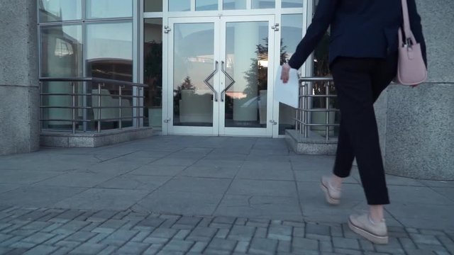 young business women in black jacket walking on the street with paper document in hands, close up legs and hends with paper