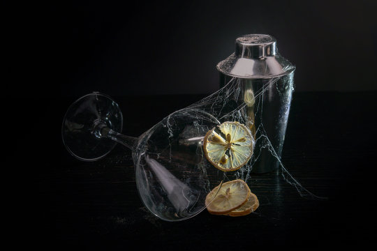 Cocktail glass, cocktail shaker and dried lemon covered in cobwebs