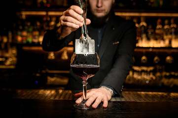 Bartender putting big ice cube in a cocktail