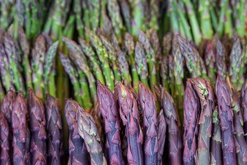 A close up of green and purple asparagus for sale on a market stall