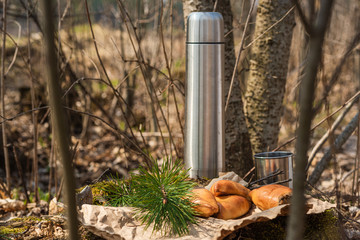 Fresh homemade meat patty cakes, thermos bottle and steel cup on stump in the forest. Picnic. Close up