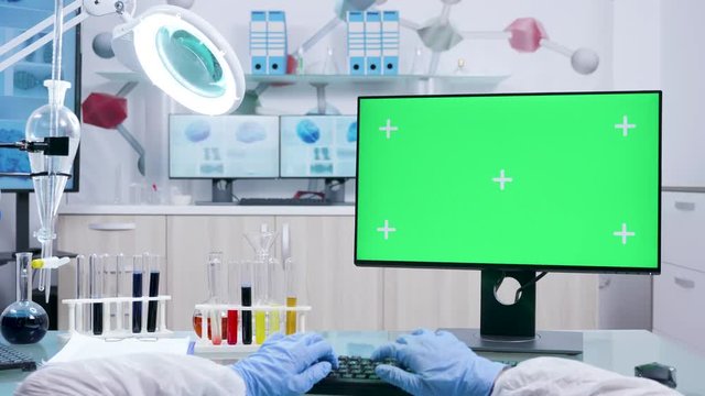 POV shot of chemist in white coverall typing on computer keyborad with green screen mock-up. Advanced modern research facility