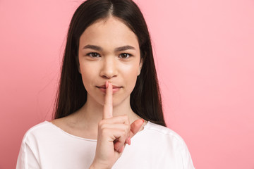 Naklejka premium Portrait closeup of teen cute girl with long dark hair holding index finger on lips and asking to be quiet