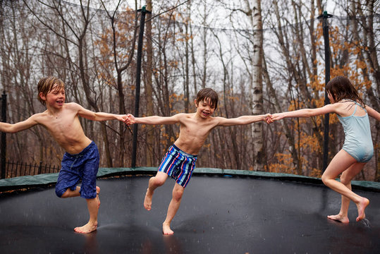 Three children jumping on a trampoline in the rain