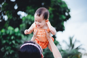 Naklejka premium Mother raised her happy little baby in her arm above her head