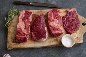 Raw black angus prime beef steak variety on vintage cutting board with rosemary, sea salt and spices
