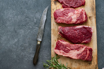 Raw black angus prime beef steak variety on vintage cutting board with rosemary, sea salt and spices