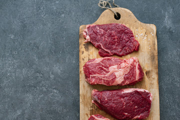 Raw black angus prime beef steak variety on vintage cutting board with rosemary, sea salt and spices