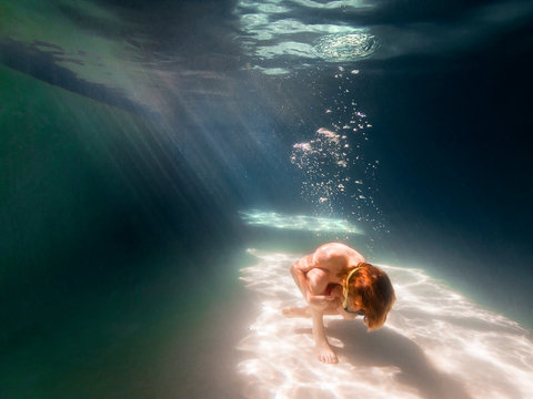 Boy curled up on the bottom of a swimming pool
