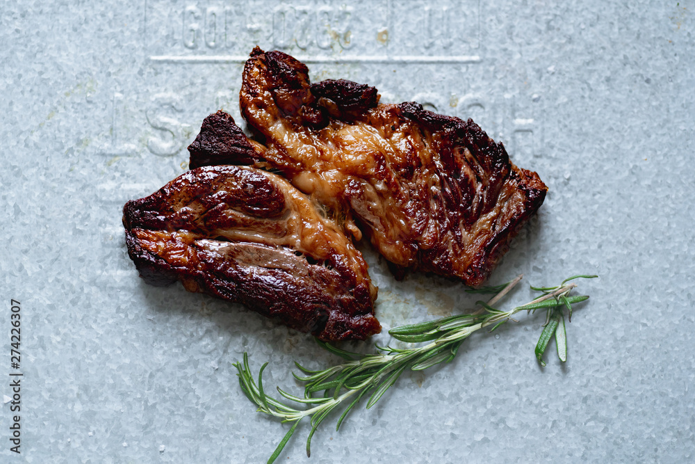 Wall mural Cooked black angus prime beef steak with rosemary and olive oil shot on metallic tray