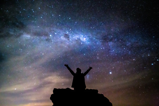 Silhouetted person hails the cosmos milky way starry night sky