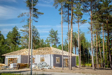 Private home house being built, work in progress, gray brick walls up and timber roof truss in lush...