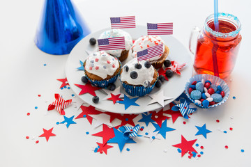 independence day, celebration and holidays concept - glazed cupcakes or muffins decorated with american flags, juice in mason jar mug, stars and red blue candies at 4th july party