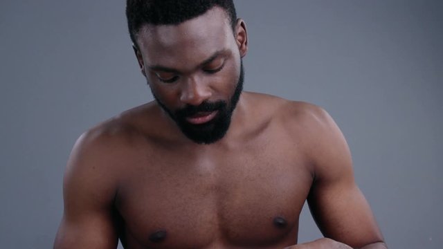 Handsome african man applying shaving cream on his beard in front of a mirror. Portrait of black male model with creamy lather on face against grey background.