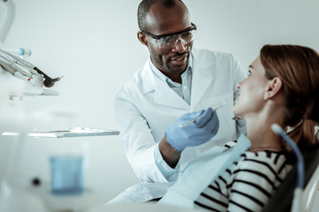 Concentrated dark-skinned doctor curing his female patient teeth