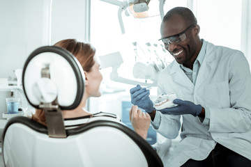 Openly-smiling dentist carrying plastic model of the jaw