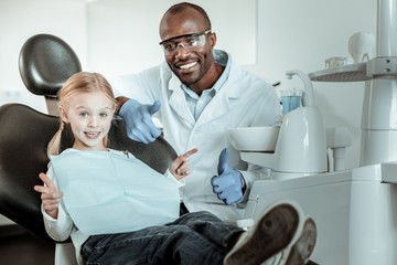 Obraz premium African American dentist in full uniform sitting behind his little patient