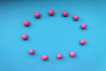 Oval shape made with small pink round candies laying in the middle of blue background. Free space for text. Invitation, postcard, banner template