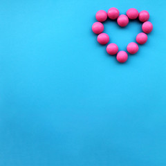 Heart shape made with small pink round candies laying on the right on the top of blue background. Free space for text. Wedding invitation, postcard, banner template