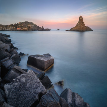 Long exposure panoramic shot of the Cyclope Island with breakwater cube blocks at the coast of Acitrezza, Sicily, Italy